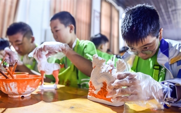 小朋友們在洛陽市孟津區(qū)朝陽鎮(zhèn)南石山村體驗(yàn)唐三彩素胎施釉技藝。圖片來源:視覺中國