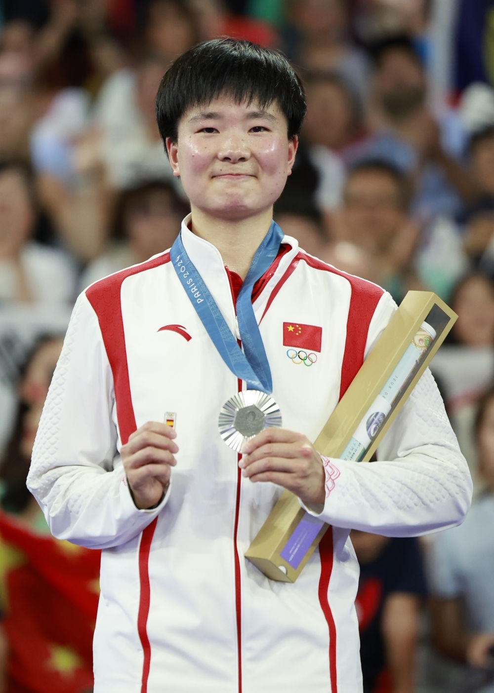 巴黎奧運(yùn)會(huì)羽毛球女子單打亞軍、中國選手何冰嬌在頒獎(jiǎng)儀式上一手握著銀牌，一手握著西班牙奧委會(huì)徽章（2024年8月5日攝）。新華社記者 任正來 攝