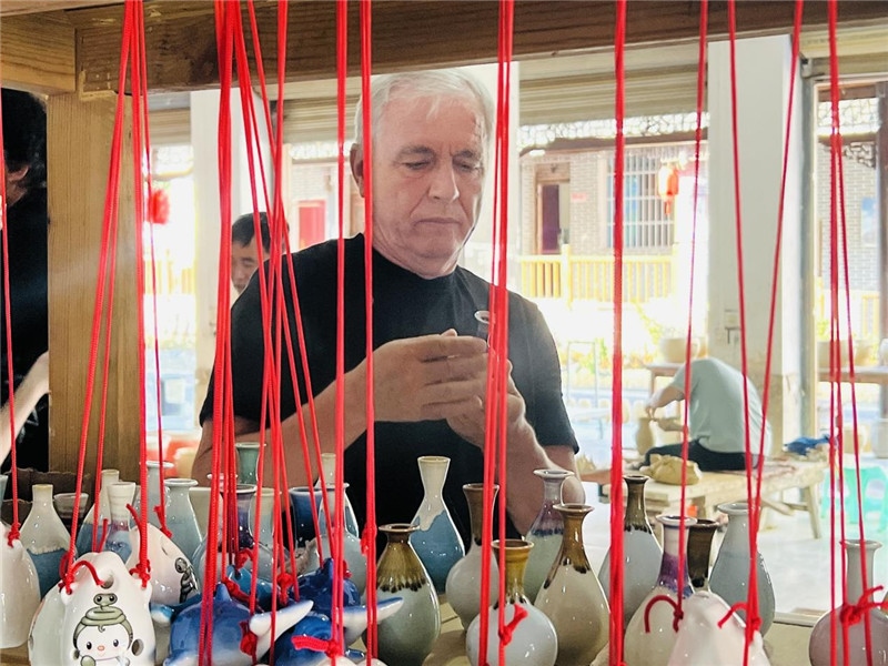 鄉(xiāng)愁如同一根根紅線，將游子與故鄉(xiāng)永遠(yuǎn)地牽連到一起。花茂村陶藝文化創(chuàng)意一條街的母氏陶藝館內(nèi)，紅線吊著陶瓶，思緒游走萬(wàn)里。摩爾多瓦“信息標(biāo)簽”通訊社社長(zhǎng)亞歷山大·塔納斯端詳著館內(nèi)展示的陶藝作品，并挑選出心儀的小擺件帶回摩爾多瓦，也帶走花茂村的“鄉(xiāng)愁”。（張亞欣攝）
