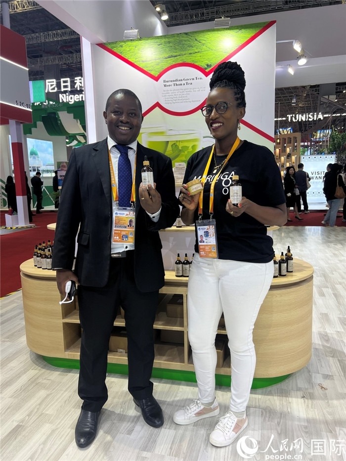6月6日，布隆迪駐華大使館一等參贊布利馬索·阿爾弗雷德 (左，Bulimaso Alfred) 和參展商卡馬里扎·埃斯特拉 (Kamariza Estella) 在第七屆中國國際進(jìn)口博覽會布隆迪館展示當(dāng)?shù)厣a(chǎn)的辣木油。（人民網(wǎng) 艾里士 攝）